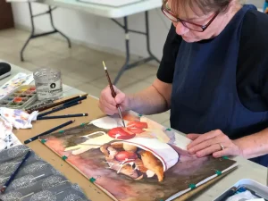 Woman painting a still life of fruits and vegetables in a bowl and on the floor during Art Class at our NW-Austin studio near Canyon Creek.