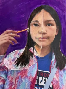 Young artist drawing half of their face over a self-photo using pastel during Art Class in South Austin, blending abstract and personal expression