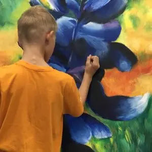 Preteen painting a blue flower in kids art class Austin