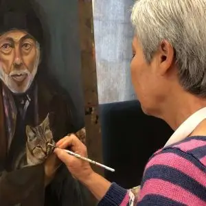 Elderly woman painting a portrait of an older man holding a cat during Austin art class, focusing on expression and detail