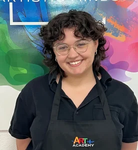 Professional portrait of art teacher with Art Plus Academy logo in the background at Southwest Austin location