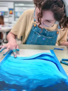 Child’s hand shading blue water with pastel during Art Class in South Austin, practicing smooth blending and color control