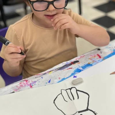 Child outlining a cat and pausing thoughtfully during Art Class in Leander, planning their next creative step