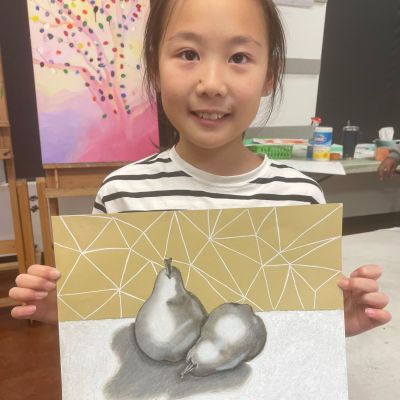 Young girl showing a realistically shaded pear with abstract background during Art Class in Round Rock