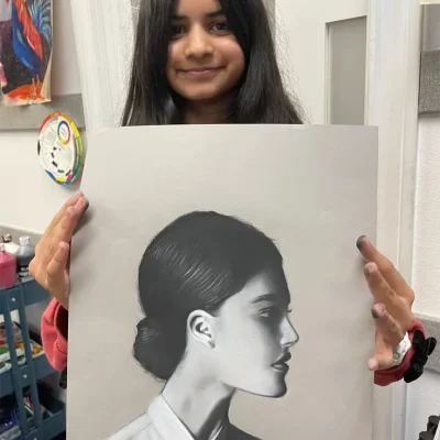 Young girl holding up a beautifully shaded realistic portrait of a woman during Art Class in Northwest Austin