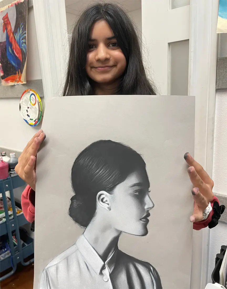 Young girl holding up a beautifully shaded realistic portrait of a woman during Art Class in Northwest Austin