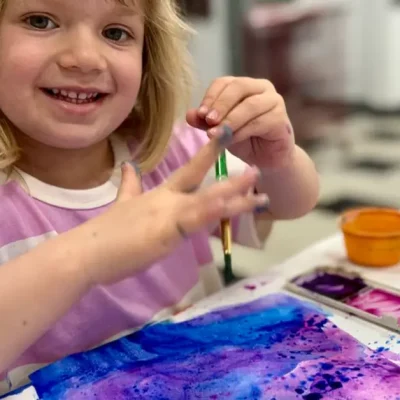 Child smiling at the camera while painting with watercolor during Fall Art Class in Northwest Austin