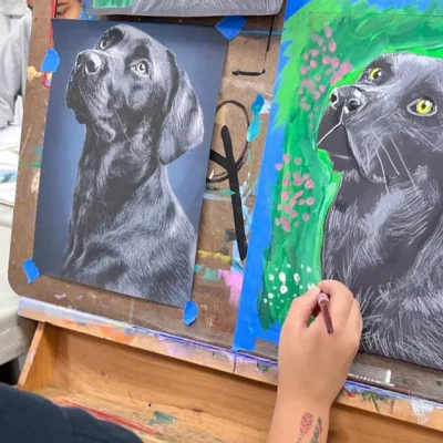 Child drawing and coloring an exceptional dog next to a reference image during Fall Art Class in Brushy Creek